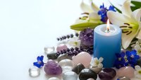Spa wellness composition with burning blue candle, healing crystals, fresh flowers and lavender for relaxation and meditation therapy.