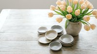 Elegant ceramic bowls arranged on rustic white wooden table with fresh peach tulips in vase, perfect for kitchen styling and home decor photography.