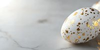 White speckled Easter egg decorated with gold metallic spots on marble background with soft focus and copy space for seasonal holiday designs.