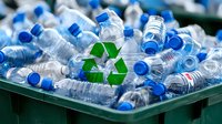 Empty plastic water bottles with blue caps collected in green recycling bin, recycling symbol visible among bottles. Environmental sustainability concept.