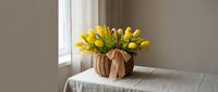 Yellow tulips in wicker basket on linen tablecloth near window. Spring flowers arrangement for home decor, interior design, seasonal decoration concepts.
