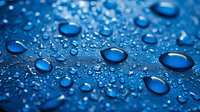 Water drops on blue waterproof surface create abstract pattern with various sized spherical droplets showing surface tension and hydrophobic effect.