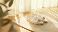 White comfortable sandals on wooden floor near window with soft natural sunlight and plant shadow creating cozy morning atmosphere. Minimalist lifestyle concept.