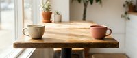Two ceramic coffee cups on rustic wooden table in bright cafe interior with plants and natural lighting for morning breakfast concept.