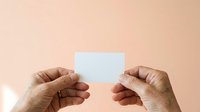 Mature hands holding blank white card on neutral beige background, suitable for business messaging, greeting cards, and promotional designs.