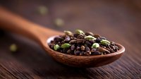 Aromatic coffee beans mixed with green cardamom pods in wooden spoon on dark rustic table, macro food photography for coffee shop menu and advertising.