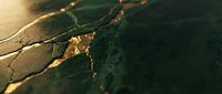 Cracked dry earth surface with golden sunlight highlighting textured soil patterns and deep fissures in drought conditions.