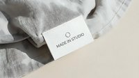 Gray linen fabric with white clothing label showing Made in Studio text on neutral beige background for branding and textile industry applications.