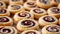 Homemade spiral cookies with raspberry jam filling arranged in rows, fresh baked shortbread swirl biscuits with sweet fruit preserve center for holiday treats.