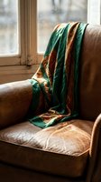 Cozy emerald green silk scarf draped over vintage leather armchair by sunny window creating warm atmospheric home interior scene for lifestyle photography.