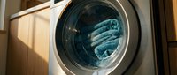 Modern front-loading washing machine with blue towels inside drum in contemporary laundry room with warm natural lighting for household cleaning concepts.