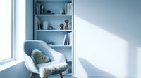 Modern minimalist reading corner with white armchair, fur pillow and built-in bookshelf in bright blue interior with natural sunlight streaming through window.
