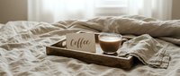 Cozy morning coffee in bed scene with wooden tray, latte cup, and handwritten card on linen bedding in warm neutral tones.