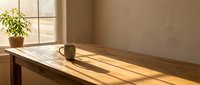 Minimalist wooden desk with potted plant and mug bathed in warm sunlight through window, creating serene workspace atmosphere for productivity and design projects.