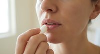 Young woman applying lip balm stick to moisturize dry chapped lips in natural daylight for skincare and beauty routine.