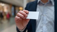 Businessman holding blank white business card mockup in office hallway. Close up of male hand showing empty card template for corporate branding design.
