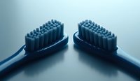 Two blue toothbrushes facing each other on reflective surface, creating symmetrical composition for dental hygiene and oral care advertising.