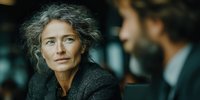 Mature businesswoman with gray hair in professional meeting discussing strategy with male colleague in modern office environment.
