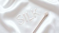 Silk text embossed on luxurious white fabric with cosmetic brush, representing skincare, beauty products, and luxury cosmetics for advertising and packaging design.