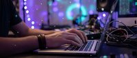Young professional working on laptop computer in modern office with colorful bokeh lights background. Technology workspace concept for business presentations.