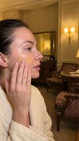 Young woman applying golden face mask in luxury hotel spa room wearing white bathrobe for skincare routine and wellness treatment.