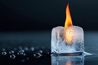 Fire and ice concept with burning flame emerging from melting ice cube on wet surface creating dramatic contrast between hot and cold elements.