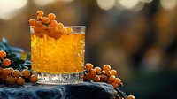 Orange cocktail in crystal glass garnished with sea buckthorn berries on dark stone surface against blurred bokeh background. Seasonal autumn drink styling.