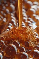 Golden honey dripping onto honeycomb surface creating bubbles and texture, macro photography with amber tones and natural light showing liquid viscosity.