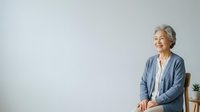 Senior woman with gray hair and light skin tone, wearing casual blue cardigan, sitting against white background with copy space for advertising and marketing campaigns.