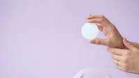 Female hands with manicured nails holding blank white circle against soft lavender background, suitable for product mockups, branding, and cosmetic presentations.