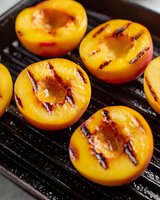 Fresh halved peaches with caramelized grill marks on cast iron grating, showing juicy flesh and natural texture in macro photography for food styling and recipes.