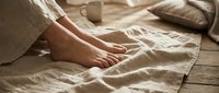 Bare feet resting on soft linen bedding in warm morning light, evoking comfort, relaxation, and cozy home lifestyle.