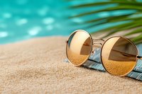 Stylish sunglasses with golden lenses resting on woven mat beside turquoise swimming pool water with palm frond shadow creating tropical vacation atmosphere.