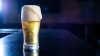 Fresh cold beer glass with foam head on dark bar counter with dramatic lighting for restaurant and pub advertising campaigns.