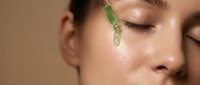 Young woman applying green facial serum with dropper for skincare routine. Natural beauty treatment with organic cosmetic oil on glowing skin.