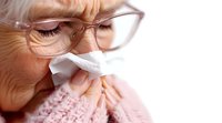 Senior Caucasian woman with glasses blowing nose into tissue, showing cold and flu symptoms in close-up view wearing pink sweater, health concept.