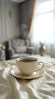 Steaming cup of hot coffee on a white saucer resting on soft bed linen in an elegant, light-toned bedroom interior.