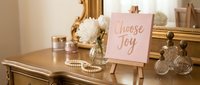 Elegant gold vanity table with Choose Joy inspirational sign, white flowers, pearls and vintage perfume bottles for feminine home decor and motivation.