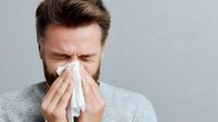 Young Caucasian man with beard sneezing into tissue, showing cold flu symptoms, healthcare concept for allergy season and respiratory illness prevention.