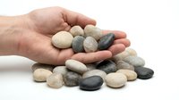 Hand holding smooth river stones with scattered pebbles on white background, isolated for spa wellness meditation and natural therapy design concepts.