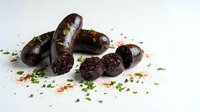 Dark chocolate blood sausage slices with fresh herbs and paprika seasoning on white background, traditional European delicacy for gourmet cooking.