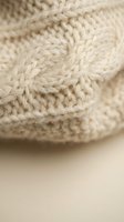 Close-up macro shot of cream colored knitted wool fabric showing detailed cable knit pattern and soft texture for cozy winter fashion and textile design.