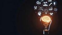 Glowing light bulb with brain filament emitting business icons representing innovation, creativity, and entrepreneurship on dark background.