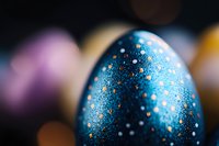 Decorative Easter egg painted in cosmic blue with silver sparkles and dots pattern on dark background with soft bokeh lights and festive atmosphere.