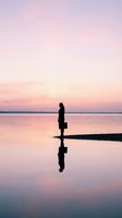 Business professional silhouette standing by calm lake at sunset with reflection in water creating peaceful contemplative scene for career concepts.