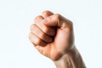 Raised clenched fist against white background showing power, strength, and determination. Dramatic lighting emphasizes muscle definition and human gesture.
