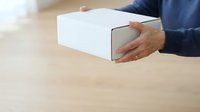 Man in dark blue shirt holding white cardboard box on wooden surface, suitable for delivery, shipping, and e-commerce concepts.