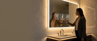 Young woman applying skincare routine in modern bathroom with illuminated mirror and marble countertop for daily beauty regimen and self-care wellness.