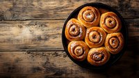 Freshly baked cinnamon rolls with sweet glaze served in black cast iron pan on rustic wooden background, top view with copy space for menu or recipe.