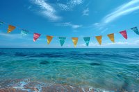 Colorful party flags hanging over turquoise ocean water against bright blue sky with wispy clouds, creating festive beach celebration atmosphere.